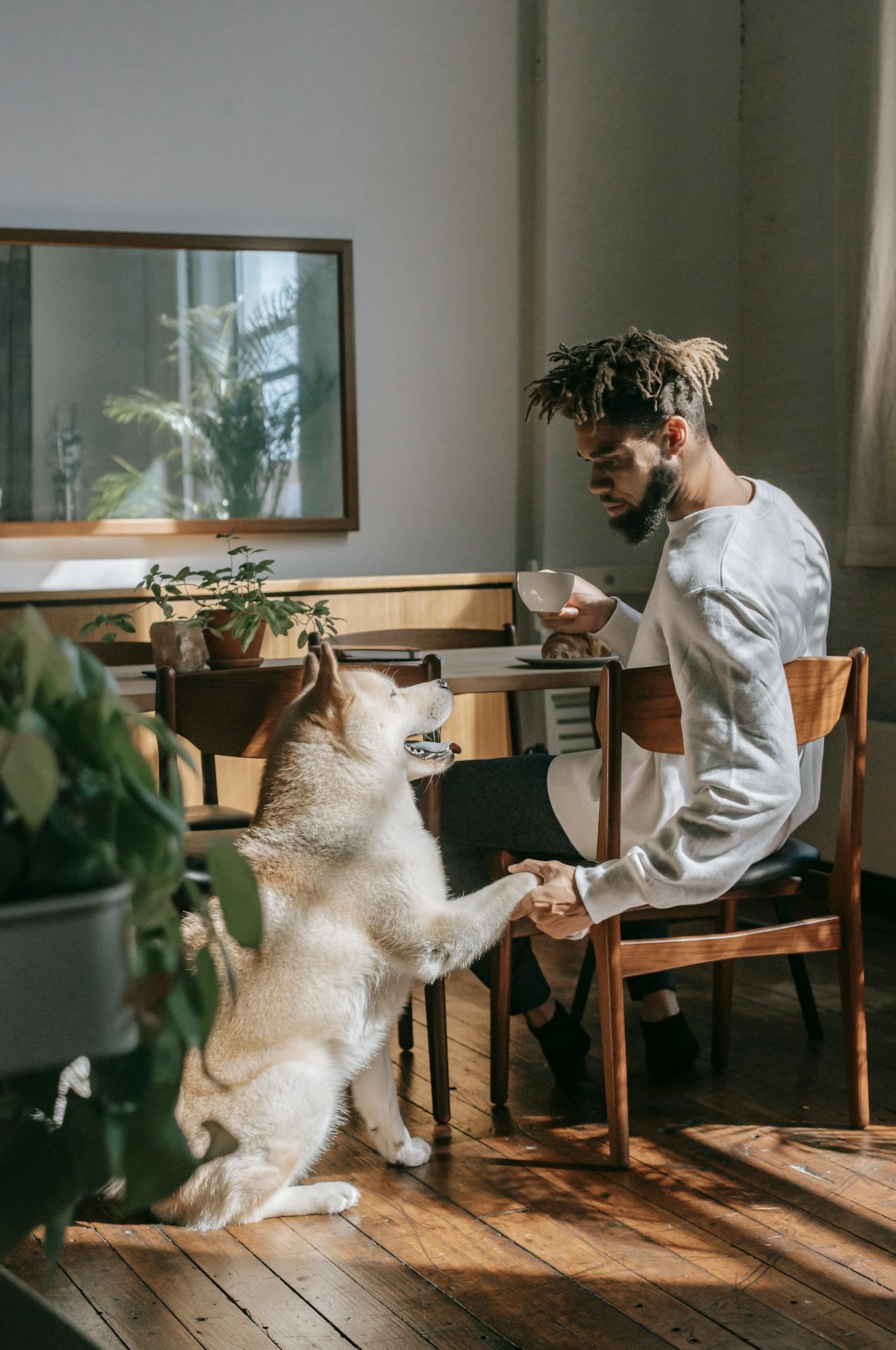 Man holding his dog’s paw while relaxing at home with a cup of tea